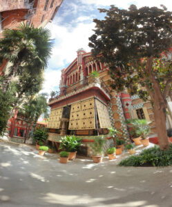 Fassadendetail der Casa Vicens mit goldenen Fensterläden, Pflanzen und Bäumen im Hof