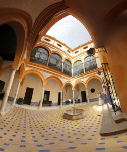 Traditioneller Patio mit gelb-orangen Rundbögen, Mosaikboden und zentralem Brunnen