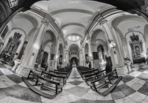 Schwarz-weiße Innenaufnahme eines Kirchenschiffs mit Säulen, Bänken und Gewölbedecke
