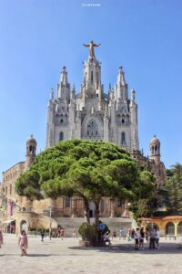 Frontansicht der Tibidabo-Basilika mit großem Baum im Vordergrund bei blauem Himmel