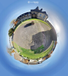 360° Tiny-Planet-Ansicht eines gepflasterten Innenhofs mit zentralem Blumenbeet, umgeben von historischen Backsteinbauten und klarem, blauem Himmel, entworfen von Yousif Karyakes Architect.