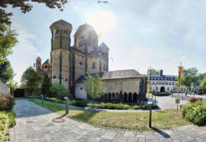 Weitwinkelaufnahme der Benediktinerabtei Maria Laach mit romanischer Kirche und Klostergebäuden unter strahlender Sonne, umgeben von gepflegten Grünflächen und Wegen.