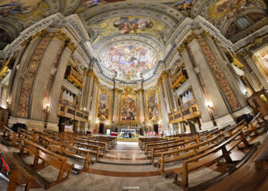 Innenansicht einer opulenten barocken Kirche in Rom mit prunkvollen Deckenfresken, vergoldeten Säulen, Bänken und einem reich verzierten Altar.