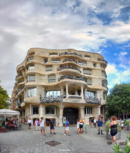 Die organisch geformte Fassade der Casa Milà (La Pedrera) von Antoni Gaudí in Barcelona mit Balkonen und Fenstern, umgeben von Menschen auf einem öffentlichen Platz.