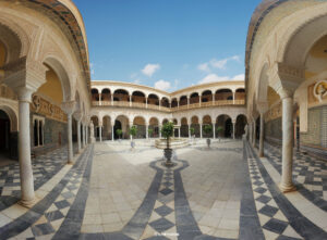 Weitwinkelaufnahme des prächtigen Patio Principal der Casa de Pilatos in Sevilla mit Bögen, Säulen, kunstvollen Fliesen und einem zentralen Brunnen unter blauem Himmel.