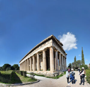 Rundblick auf den gut erhaltenen Tempel des Hephaistos in Athen mit dorischen Säulen, Besuchern im Vordergrund und klarem Himmel über umliegenden Bäumen.