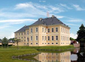 Historisches gelbes Schloss mit weißen Fensterläden am Wasser, umgeben von grünem Rasen und Bäumen unter blauem Himmel.