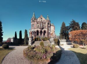Historisches Schloss mit Türmen und Garten im Herbst bei klarem Himmel. Der Weg führt zum Gebäude, umgeben von Bäumen und Pflanzen.