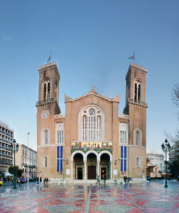 Blick auf eine prunkvolle Kathedrale mit zwei Glockentürmen, buntem Mosaik über drei Rundbögen und gepflastertem Platz im Vordergrund.