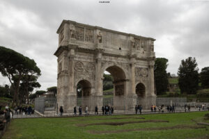 Der imposante Konstantinsbogen in Rom, ein antikes römisches Triumphbogenmonument mit Reliefs und Skulpturen, umgeben von Grünflächen und Touristen unter bewölktem Himmel.