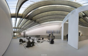 Innenansicht einer weitläufigen, modernen Ausstellungshalle des MAXXI Museums mit geschwungenen Decken, Oberlichtern und abstrakten Skulpturen auf hellem Boden.
