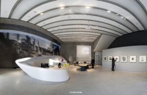 Innenansicht des MAXXI Museums in Rom mit einem geschwungenen weißen Empfangstresen, moderner Architektur und Kunstausstellungen an den Wänden.