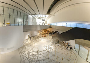 Innenaufnahme des MAXXI Museums in Rom, die die dynamische Architektur mit geschwungenen Wänden, Rampen und einer großen Installation im Zentrum zeigt.