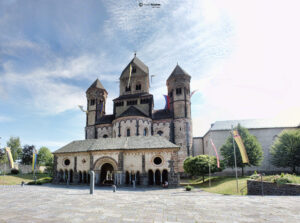 Frontale Ansicht der romanischen Abteikirche Maria Laach mit ihren markanten Türmen und dem Narthex unter leicht bewölktem Himmel.