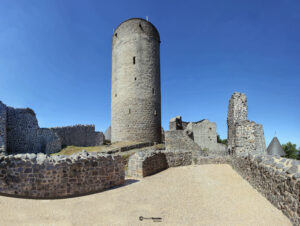 Weitwinkelansicht der historischen Nürburg in der Eifel mit zentralem, hohem Rundturm und weitreichenden Steinmauern unter strahlend blauem Himmel.