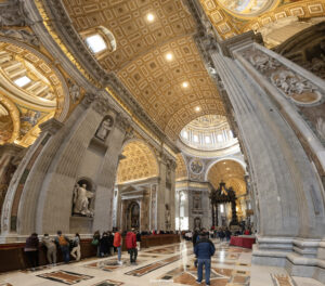 Weitwinkelaufnahme des prächtigen Innenraums des Petersdoms im Vatikan mit detailreicher goldener Kassettendecke, Marmorsäulen und dem Baldachin von Bernini.