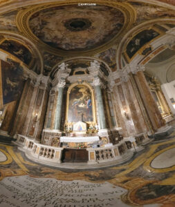 Innenansicht einer prachtvollen römischen Kirche mit detailreichen Fresken an der Decke, vergoldeten Verzierungen und Marmorsäulen, die einen Altar umrahmen.
