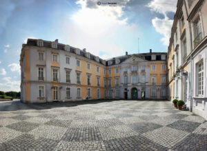 Elegantes Schloss im Barockstil mit weiten Innenhof und Sonnenschein. Historisches Gebäude und gepflasterter Boden.
